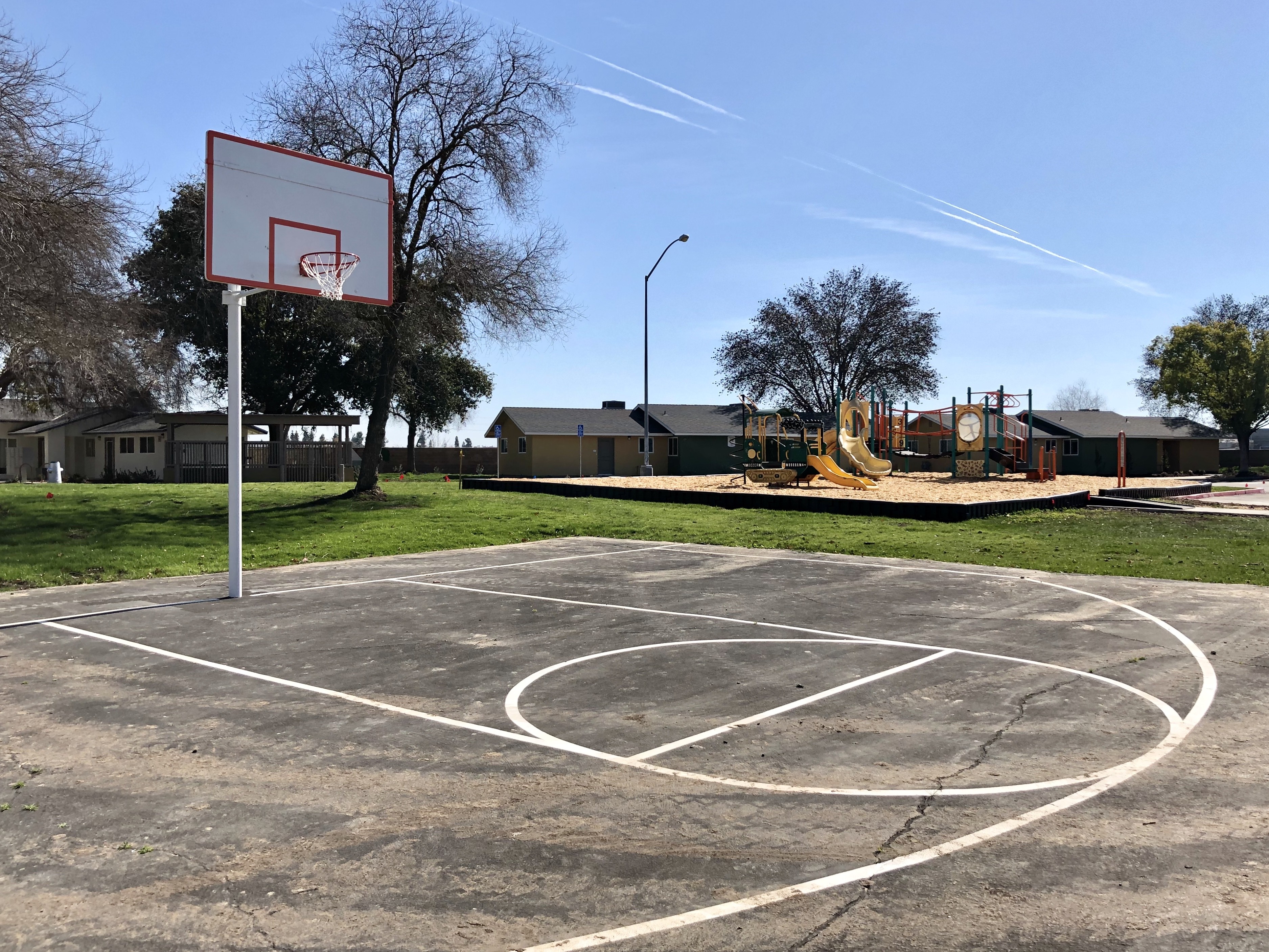 A basketball court with a hoop and a playground in the background.